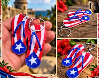 Puede incluir: Un par de llaveros con forma de chanclas que presentan el diseño de la bandera de Puerto Rico con rayas rojas y blancas, un triángulo azul y una estrella blanca. Los llaveros tienen tiras azules y una anilla metálica plateada.