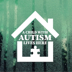 May include: A white house-shaped sticker with the text "A child with autism lives here" and a jigsaw piece inside. The sticker is on a green background with water droplets.