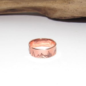 May include: A copper ring with a mountain and tree design engraved on the band.