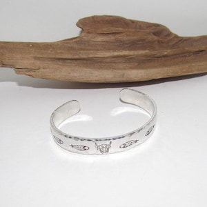 May include: Silver bracelet with a hammered finish and engraved designs of feathers and a buffalo head.