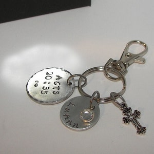 K&ouml;nnte beinhalten: Silberner Schl&uuml;sselanh&auml;nger mit drei Anh&auml;ngern. Der erste Anh&auml;nger ist ein rundes Metallschild mit dem Text "ACTS 20:35". Der zweite Anh&auml;nger ist ein rundes Metallschild mit dem Text "I AM IN". Der dritte Anh&auml;nger ist ein kleines silbernes Kreuz.