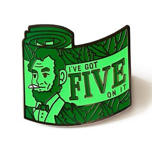 May include: Green enamel pin featuring a cartoon illustration of Abraham Lincoln with a beard and a cigarette, holding a rolled-up bill of money. The text "I've got FIVE on it" is written on the pin.
