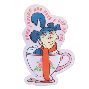 May include: A sticker featuring a cartoon creature with blue fur and an orange scarf, sitting in a teacup. The teacup is pink with a floral design. Text on the sticker reads "COME INSIDE AND HAVE A CUP OF TEA."