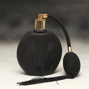 Puede incluir: Un frasco de perfume vintage negro con un atomizador dorado y una pera negra. La botella tiene forma redonda con un diseño de tulipanes grabado en la parte delantera. La pera tiene una borla negra.