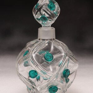 May include: A clear glass perfume bottle with a diamond-patterned design and a matching stopper. The bottle features teal-coloured circular accents. The stopper is frosted, and the bottle has a classic, elegant design.