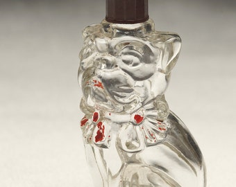 May include: Clear glass bulldog-shaped bottle with a dark brown cap. The bottle has red accents on the collar and face. The bulldog is sitting upright, with its paws in front.