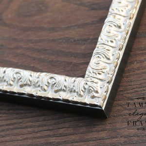 Puede incluir: Un marco de fotos plateado con un dise&ntilde;o ornamentado y en relieve. El marco est&aacute; sobre una superficie de madera oscura. El texto "TAMMY'S elegant FRAMES" es visible en la esquina inferior derecha de la imagen.