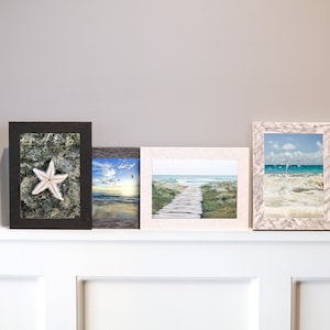 May include: Four framed pictures of beach scenes. The frames are all different colors and styles. The pictures show a starfish, a beach with a boardwalk, a beach with waves crashing, and a beach with a sunset.
