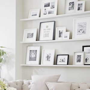 May include: A white wall with two shelves displaying black and white framed photos and a framed print with the text "Do small things with great love".