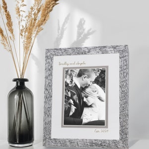 May include: A rectangular picture frame with a textured gray and white finish containing a black and white photograph of a couple. The frame features the printed text "Bradley and Angela" at the top and "Est. 2024" at the bottom in a script font.