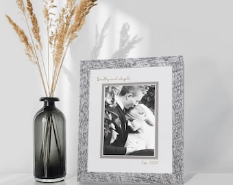 May include: A rectangular picture frame with a textured grey and white finish containing a black and white photograph of a couple. The frame features the printed text "Bradley and Angela" at the top and "Est. 2024" at the bottom in a script font.