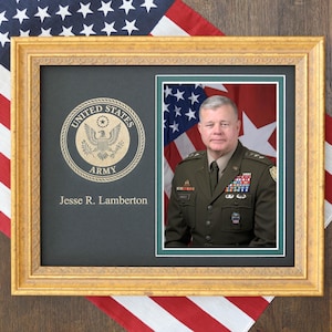 May include: A framed portrait featuring a man in a military uniform, set against a backdrop of the American flag. The frame is gold-colored, and the portrait includes the United States Army emblem and the name "Jesse R. Lamberton."