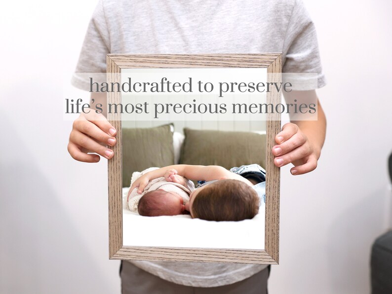 Puede incluir: Una fotograf&iacute;a enmarcada de dos hermanos, un ni&ntilde;o mayor sosteniendo a un beb&eacute; m&aacute;s peque&ntilde;o. La foto est&aacute; en un marco de madera clara con un paspart&uacute; blanco. El texto "handcrafted to preserve life's most precious memories" est&aacute; impreso sobre el marco.