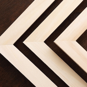 May include: Close-up of several unfinished wooden picture frames arranged in a chevron pattern. The frames are light-colored, and the background is a dark brown, creating a contrast. The image highlights the geometric design.