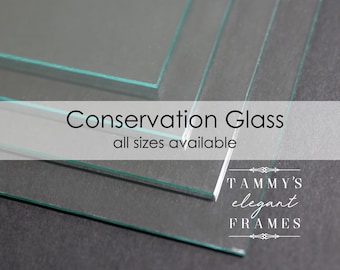 May include: Close-up of several pieces of clear conservation glass, stacked on top of each other. The text "Conservation Glass" and "all sizes available" is printed on a white banner in front of the glass. The text "TAMMY'S elegant FRAMES" is printed below the glass.