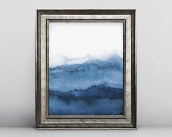 May include: A framed watercolor print featuring abstract blue and white mountain-like shapes. The artwork is encased in a silver-colored, ornate frame. The painting's color palette ranges from deep indigo to light blue, creating a serene and calming aesthetic.