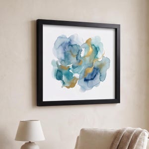 May include: Square framed art print featuring an abstract watercolor design. The artwork showcases flowing blue and teal hues with gold accents. The print is set against a white background and framed in a black border, suitable for home decor.