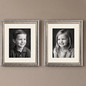 Op de afbeelding: Twee ingelijste zwart-wit portretten van kinderen. Elk portret zit in een zilveren sierlijke lijst met een cr&egrave;mekleurige passe-partout. De portretten zijn van een lachende jongen en een lachend meisje.