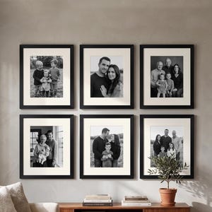 May include: Six framed black and white family portraits are displayed on a gray wall. Each portrait is in a black frame with a white mat. The portraits feature various family groups, creating a gallery wall arrangement.