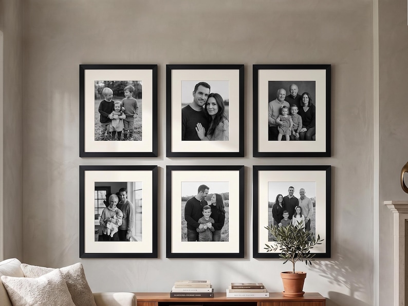 May include: Six framed black and white family portraits are displayed on a gray wall. Each portrait is in a black frame with a white mat. The portraits feature various family groups, creating a gallery wall arrangement.