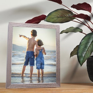 Puede incluir: Una fotograf&iacute;a enmarcada de dos ni&ntilde;os de pie en una playa, mirando hacia el oc&eacute;ano. El ni&ntilde;o est&aacute; se&ntilde;alando hacia la derecha y la ni&ntilde;a est&aacute; sujetando el brazo del ni&ntilde;o. El marco es de madera clara.
