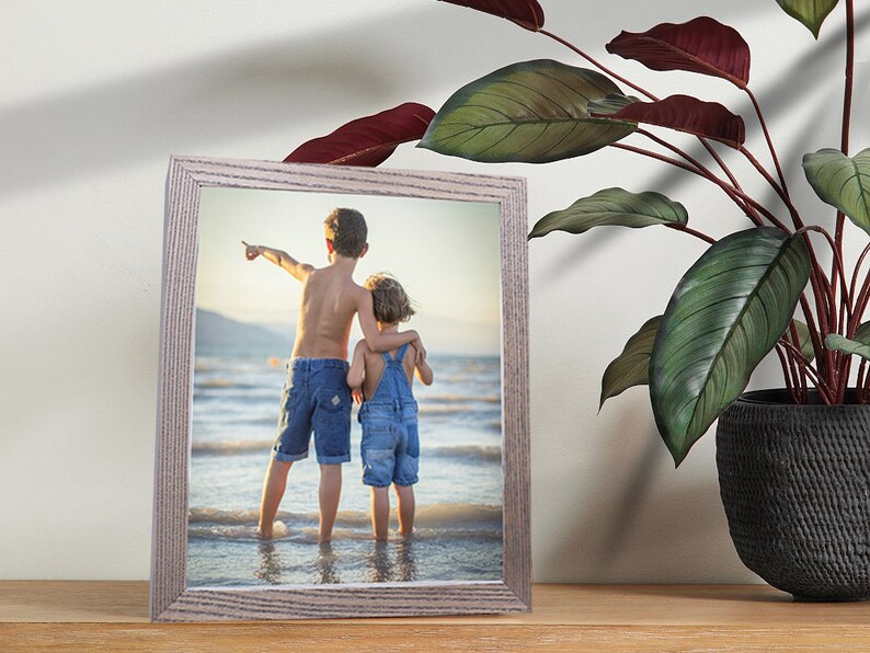 Puede incluir: Una fotograf&iacute;a enmarcada de dos ni&ntilde;os de pie en una playa, mirando hacia el oc&eacute;ano. El ni&ntilde;o est&aacute; se&ntilde;alando hacia la derecha y la ni&ntilde;a est&aacute; sujetando el brazo del ni&ntilde;o. El marco es de madera clara.
