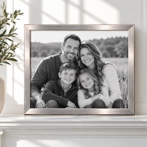 May include: A rectangular picture frame with a metallic silver finish containing a black and white photograph of a family of four. The portrait features two adults and two children smiling together in an outdoor field setting with trees visible.