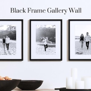 May include: Three black framed gallery wall art pieces with black and white photos of people. The text "Black Frame Gallery Wall" is above the frames. Below the frames are two black bowls and a wooden tray with candles.