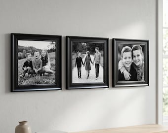 May include: Three black framed photographs of children hanging on a white wall. The photos are black and white and show children in various poses. The frames are square with a simple, elegant design. The photos are hung above a wooden surface.
