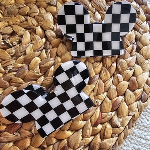 May include: Two black and white checkered mouse ear hair clips. The clips are made of plastic and have a glossy finish.