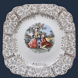 May include: A square ceramic plate with scalloped edges featuring a central colorful illustration of a couple in period clothing within a garden setting. The border is decorated with an intricate gold floral and scroll pattern on a white base.