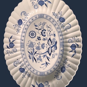 May include: An oval ceramic platter with a scalloped edge, featuring a white base and a blue floral pattern. The design includes a central bouquet of flowers and leaves, surrounded by a decorative border and individual floral motifs on the rim.