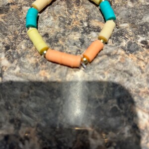 May include: A colorful bracelet made of small, cylindrical beads. The beads are arranged in a pattern of yellow, orange, and turquoise.