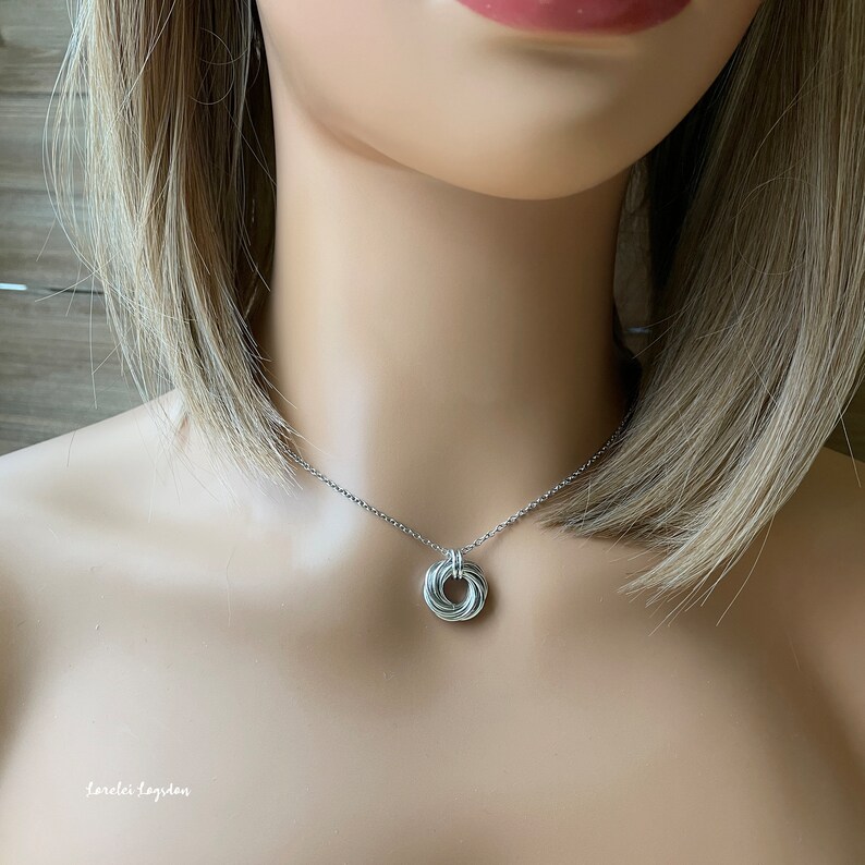 May include: A silver necklace with a circular pendant made of multiple intertwined silver wires.