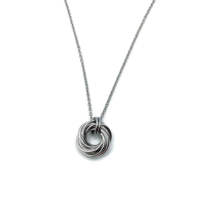May include: A silver necklace with a circular pendant made of multiple intertwined strands of metal.