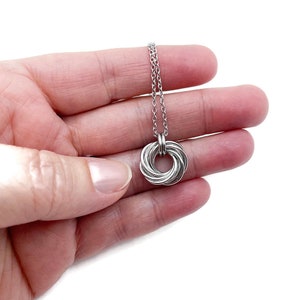 May include: A silver chain necklace with a silver infinity knot pendant. The pendant is made of multiple intertwined rings.