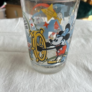 May include: Clear glass featuring Mickey Mouse at the helm of a ship's wheel, with Donald Duck and stars in the background. The glass has the text "...it was all started" at the bottom. A vintage Disney collectible.