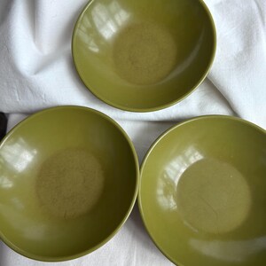 May include: Three round, olive green bowls with smooth, matte-finish interiors and slightly curved sides. Each bowl features a consistent circular shape and a uniform solid color throughout the surface, showing subtle signs of light surface wear.