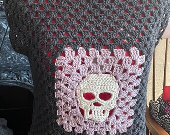 May include: A black and pink crocheted sleeveless top with a white crocheted skull design in the center.