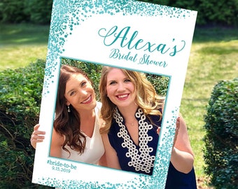 Op de afbeelding: Een teal en witte fotobooth-prop met een frame voor een foto. De tekst "Alexa's Bridal Shower" en "#bride-to-be 9.15.2019" staat op de prop gedrukt.