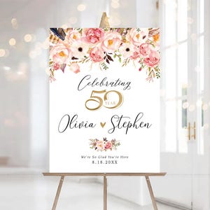 May include: A white sign on a wooden easel, with floral arrangements and text. The sign reads "Celebrating 50 Year" with the names "Olivia" and "Stephen" below. The date "8.18.20XX" is also included.