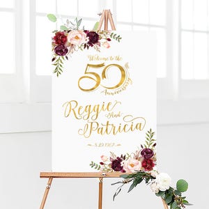 May include: Welcome to the 50th Anniversary of Reggie and Patricia, 8.29.1967. A white sign with gold lettering and burgundy floral accents.