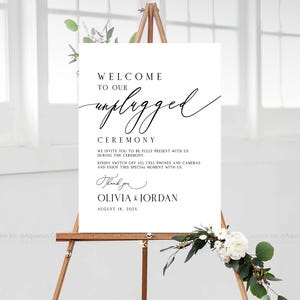 May include: A white sign on a wooden easel with the words "Welcome to our unplugged ceremony." The sign also includes a request to turn off cell phones and cameras. The names Olivia & Jordan and the date August 18, 202X are also on the sign.
