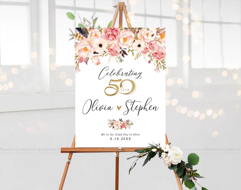 May include: A white sign on a wooden easel, adorned with pink and white floral arrangements. The sign displays "Celebrating 50 Year" with the names "Olivia & Stephen" and the date "8.18.20XX".