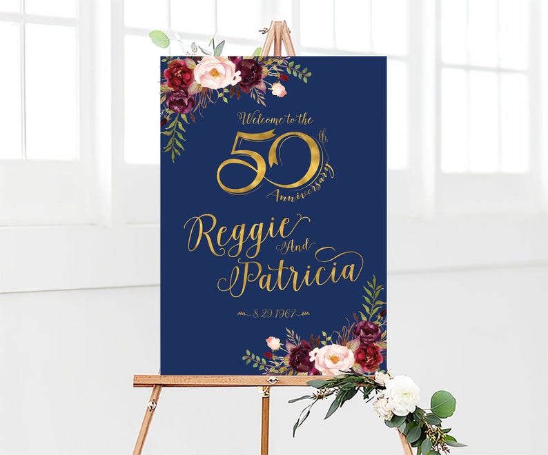 May include: A navy blue welcome sign with gold lettering announcing a 50th anniversary for Reggie and Patricia. The sign is decorated with burgundy and pink floral illustrations. The date 8.29.1967 is also included.