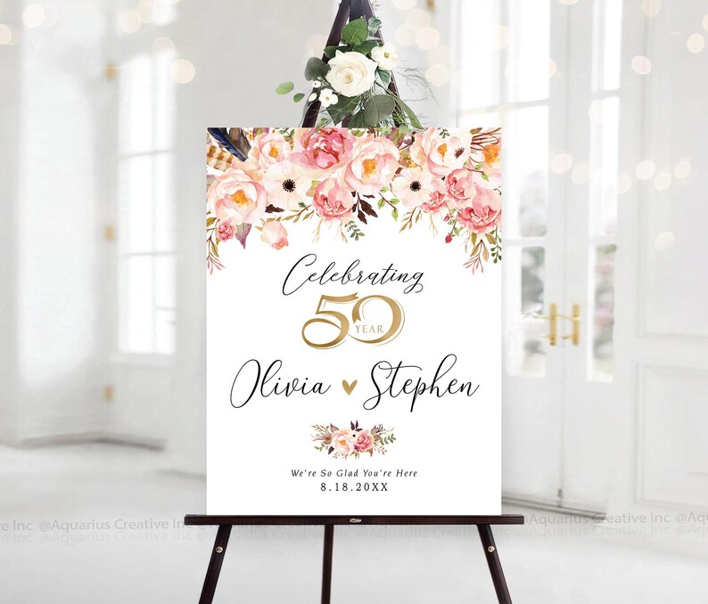 May include: A white sign on a black easel, adorned with pink and peach floral arrangements. The sign displays "Celebrating 50 Year", the names "Olivia & Stephen", and the date "8.18.20XX".