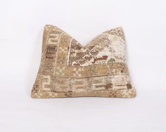 May include: A rectangular pillow with a beige and brown patterned design. The pillow has a faded, vintage look with geometric and abstract shapes. The color palette includes shades of brown, beige, and touches of green.