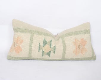 May include: Rectangular decorative pillow with a cream-colored background and floral patterns. The pillow features a woven texture with peach and green floral designs, and green borders. A cozy accent for any room.