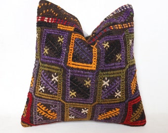 May include: A colorful, geometric patterned pillow with a brown background. The pillow is made of woven fabric and has a variety of colors, including purple, green, yellow, and red.