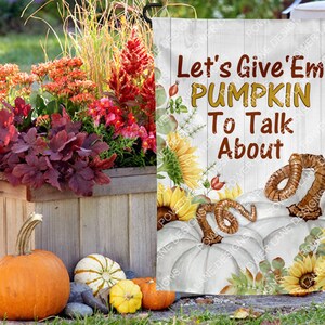 May include: A white garden flag with a fall theme. It features a white pumpkin with a brown worm on top. The text on the flag reads "Let's Give 'Em Pumpkin To Talk About".